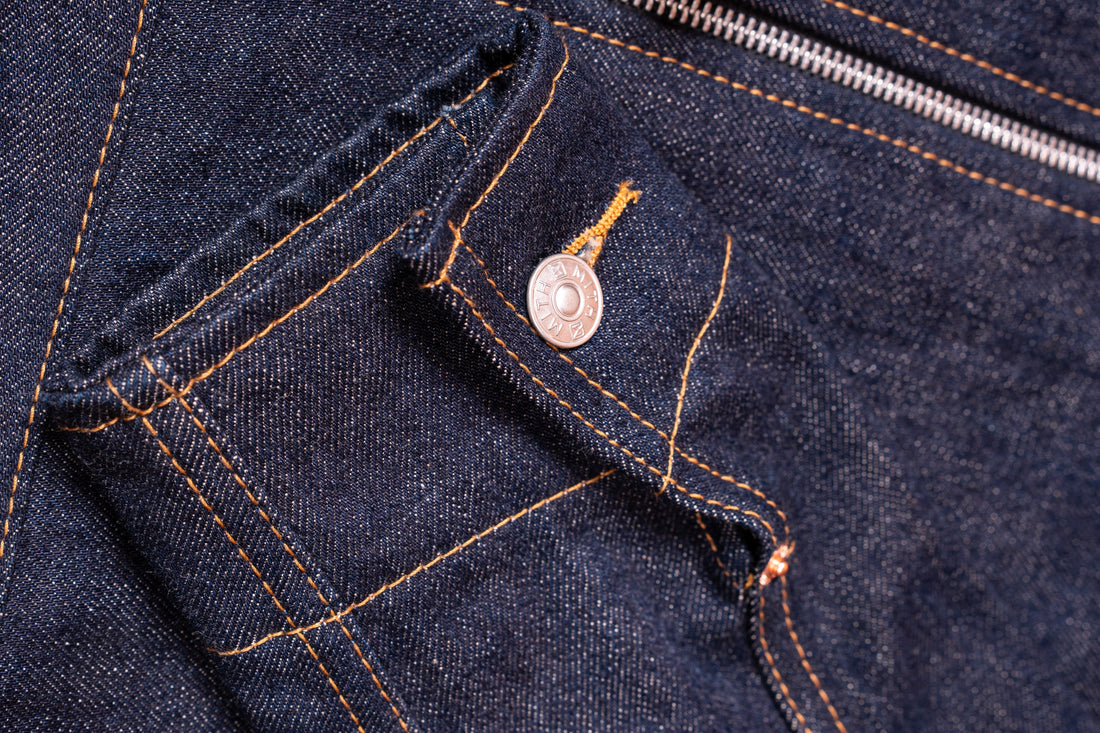 Close-up of raw indigo denim with Mith rivet, coin pocket and orange stitching