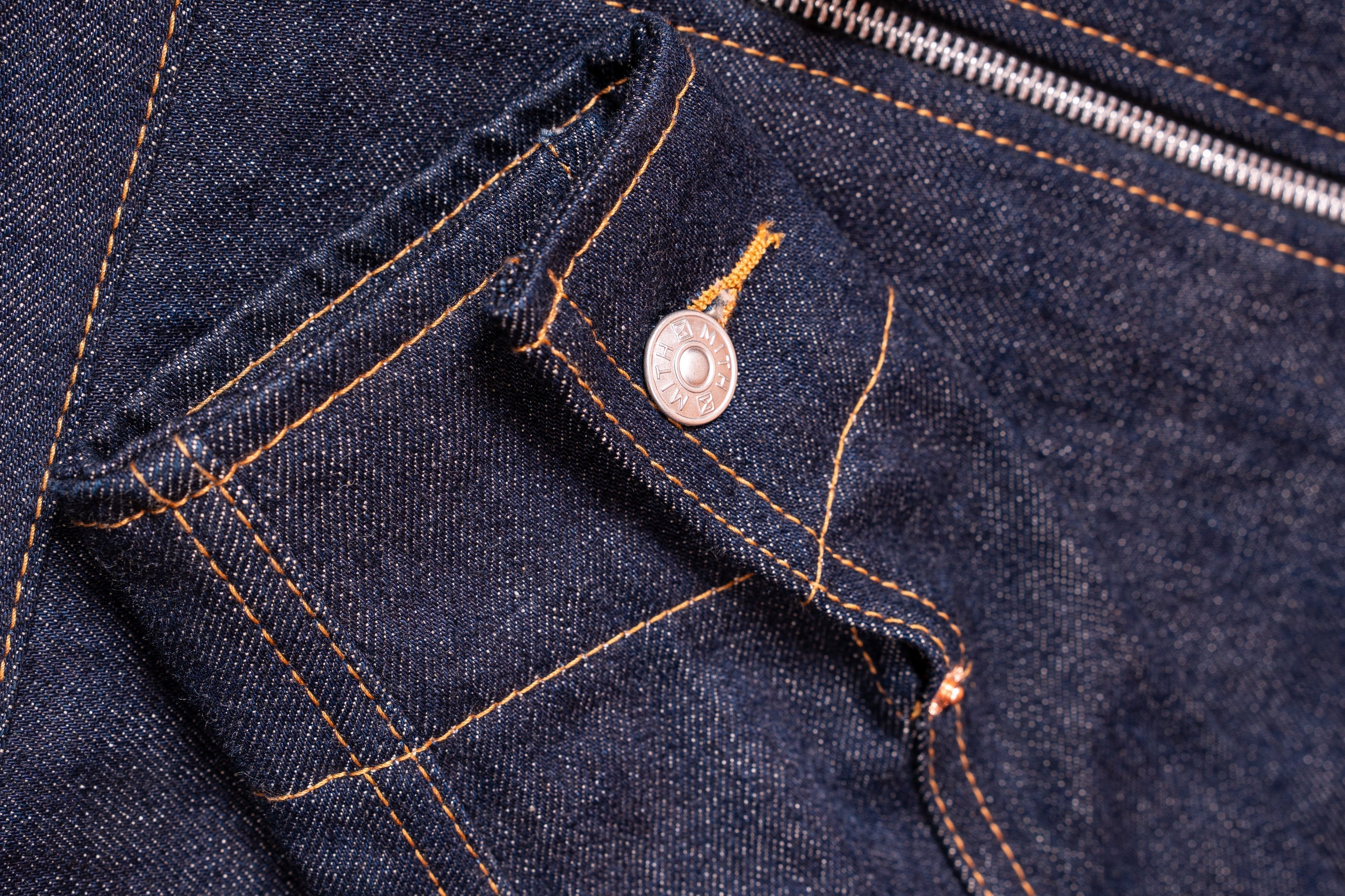 Close-up of raw indigo denim with Mith rivet, coin pocket and orange stitching