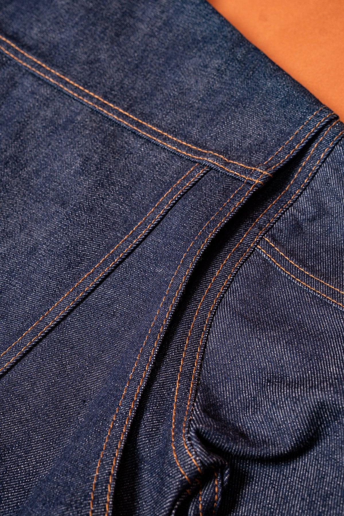 Close-up of raw indigo denim seam and construction detail on orange background