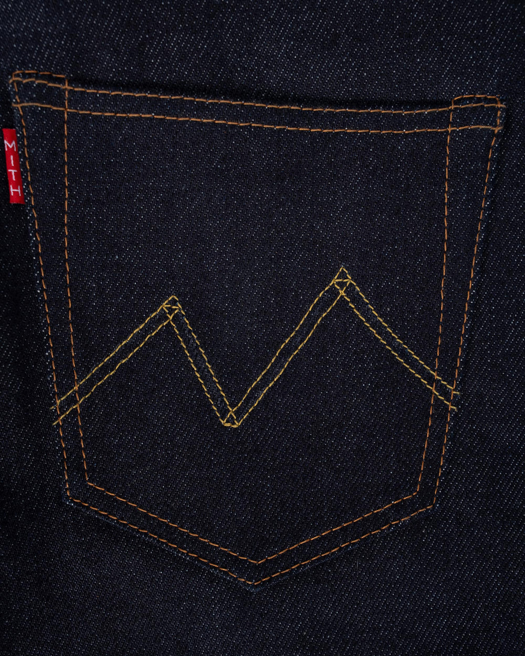Close-up of 16oz indigo denim back pocket with a subtle tonal zigzag stitch detail (Mt. Everest) and a small red Mith brand tab on the left edge
