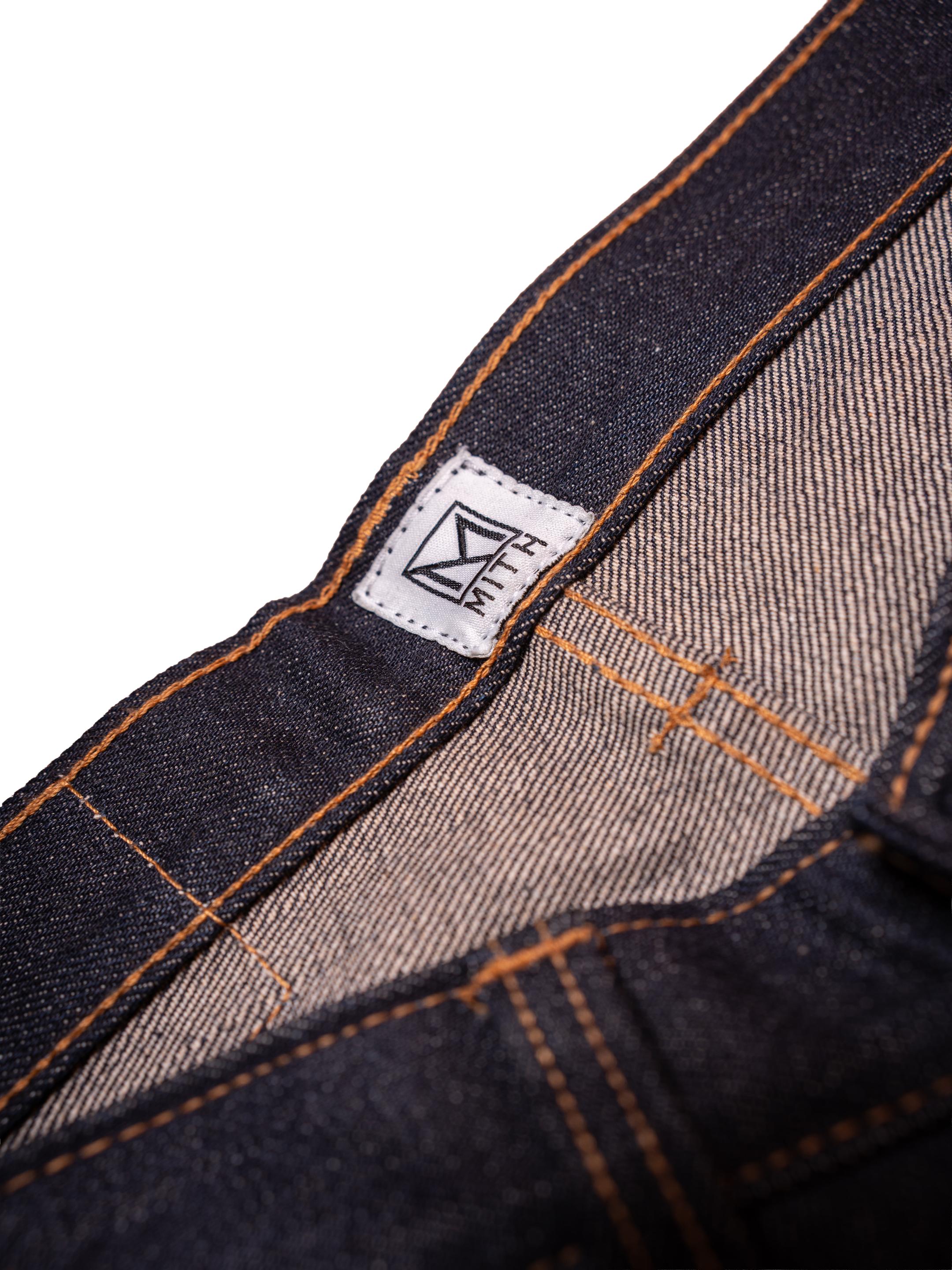 Close-up of a denim fabric with stitching details and a brand label on a white background