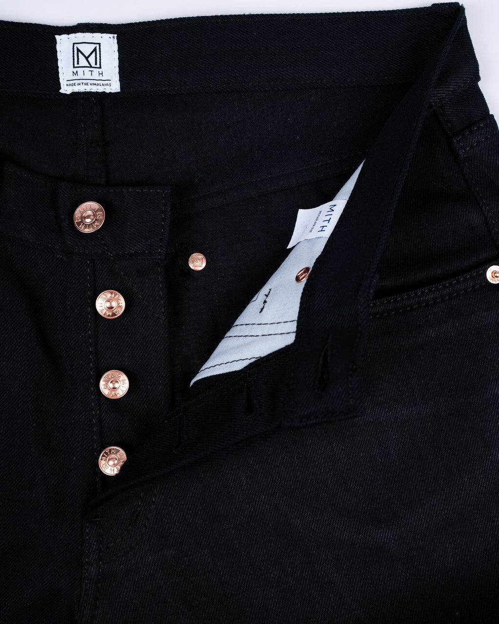 Close-up of 17oz black denim jeans showing the waistband, button fly, and buttons, with a white inner label visible.