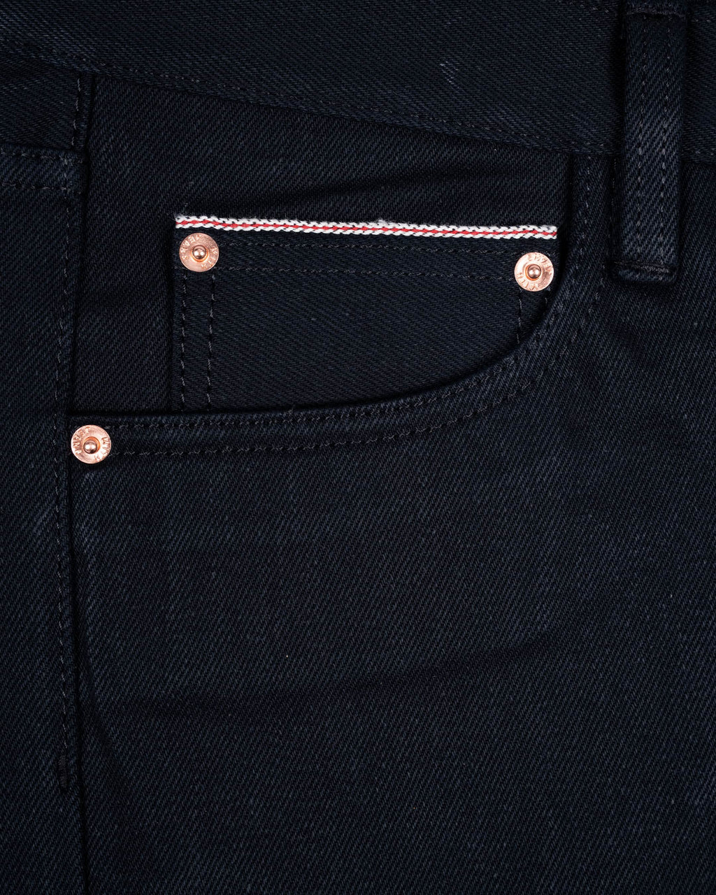 Close-up of 17oz black selvedge denim jeans showing the front pocket with copper-toned rivets and selvedge id.