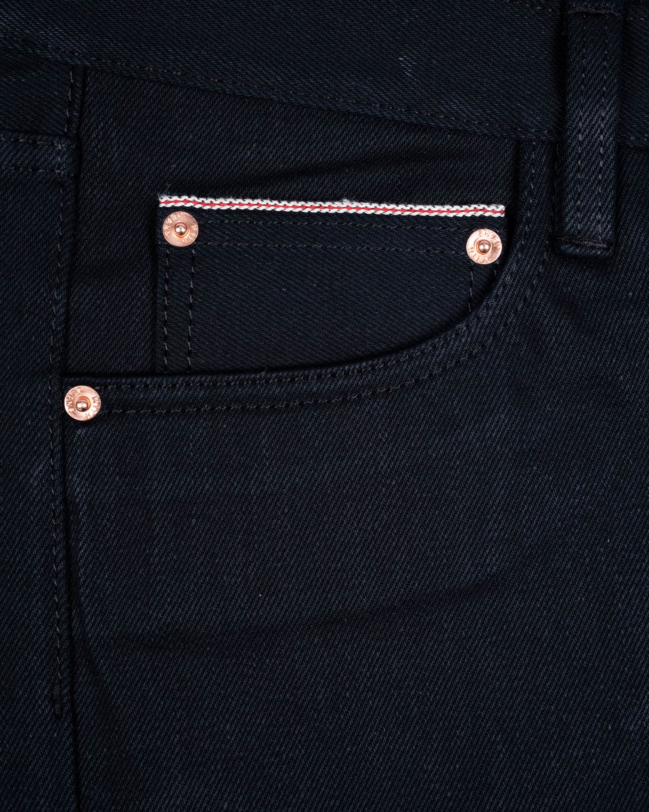 Close-up of 17oz black selvedge denim jeans showing the front pocket with copper-toned rivets and selvedge id.
