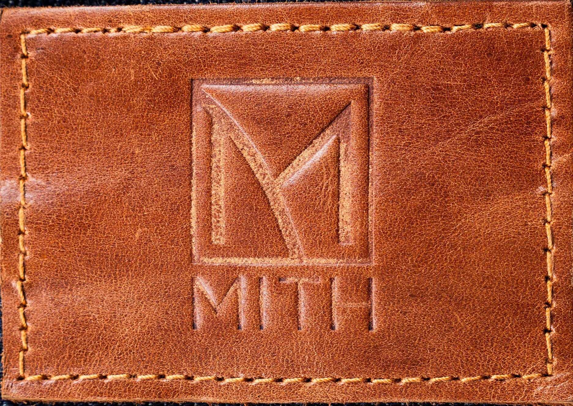 Close-up of a brown leather patch with a stitched border and an embossed MITH logo.