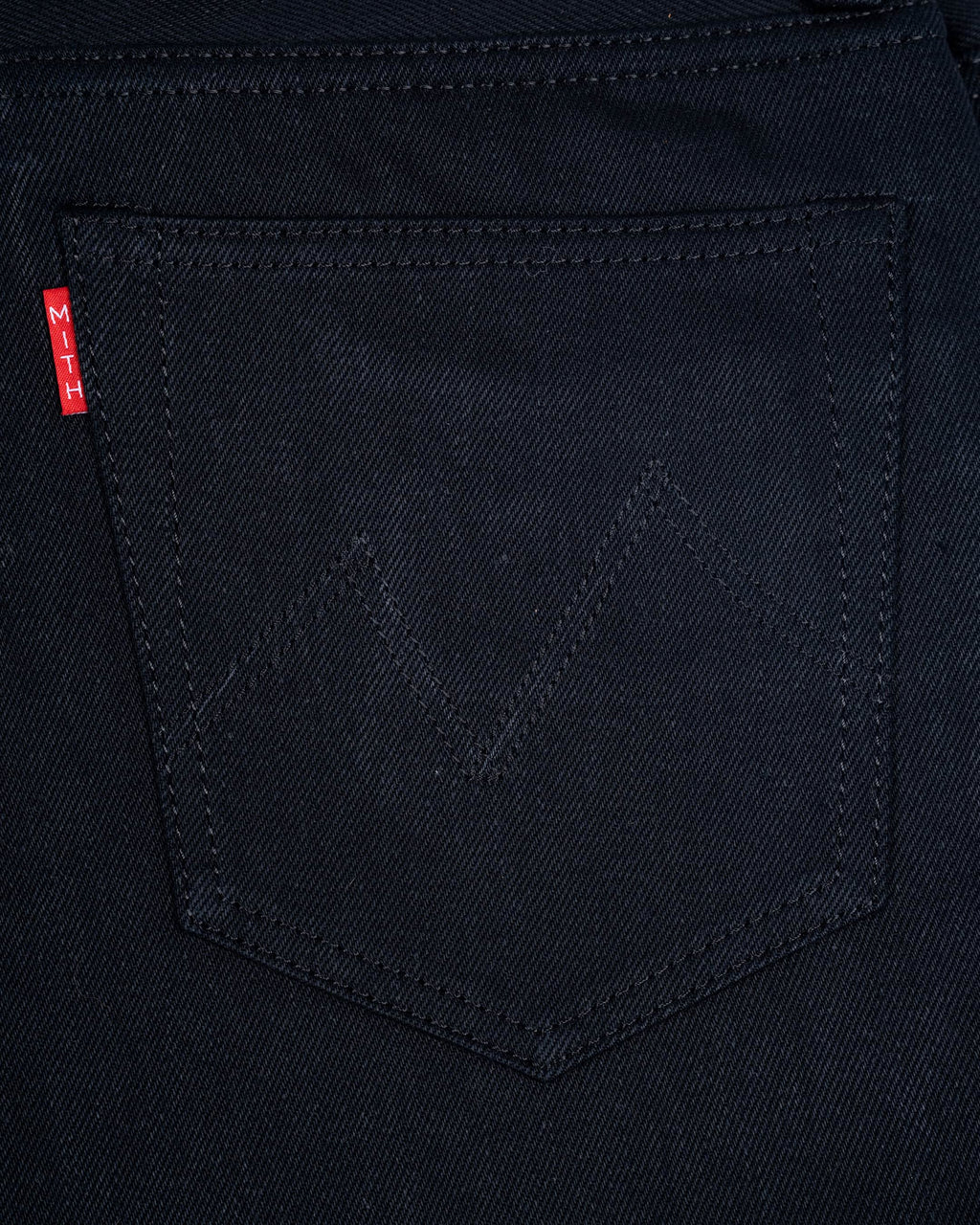 Close-up of a17oz black denim back pocket with a subtle tonal zigzag stitch detail(Mt. Everest) and a small red Mith's brand tab on the left edge.
